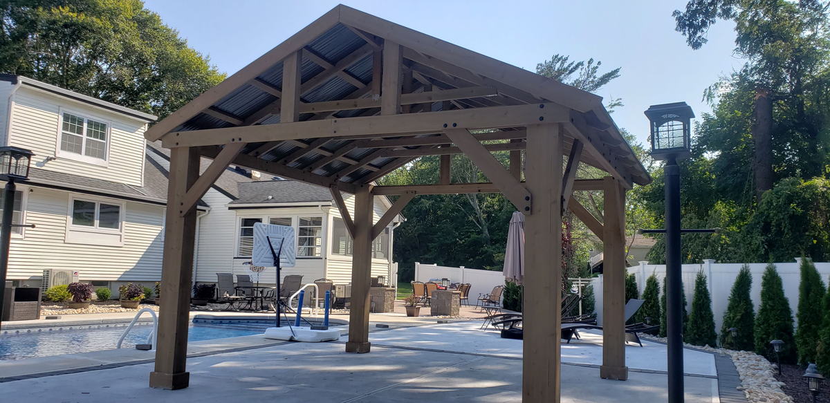 Finished cedar timber-frame pavilion with a metal roof beside an in-ground pool
