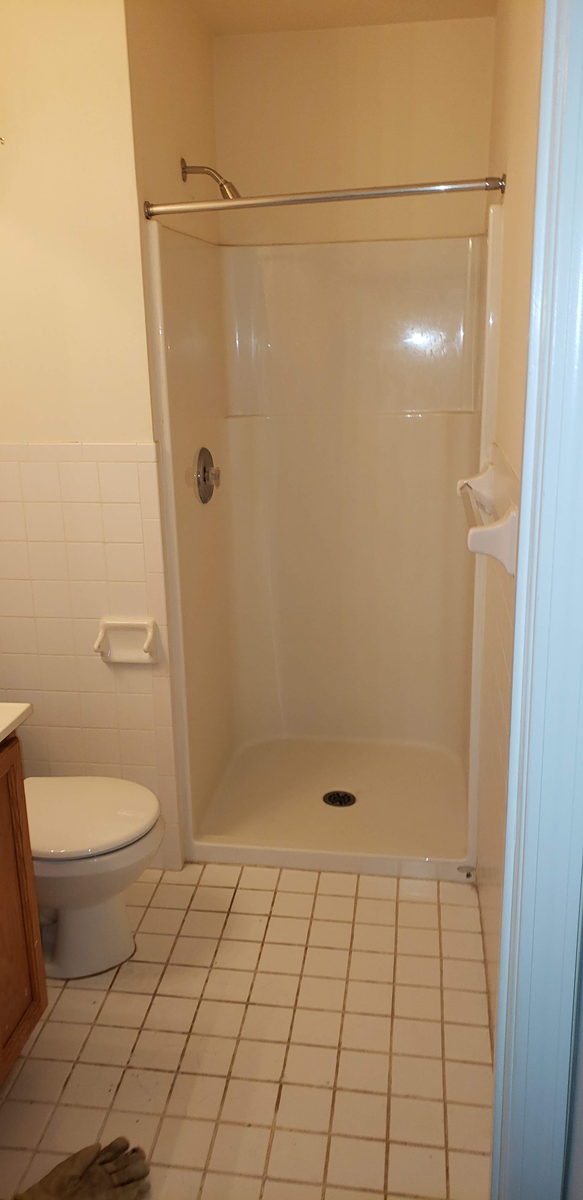 Dated pink bathroom with a fiberglass shower stall and beige floor tile