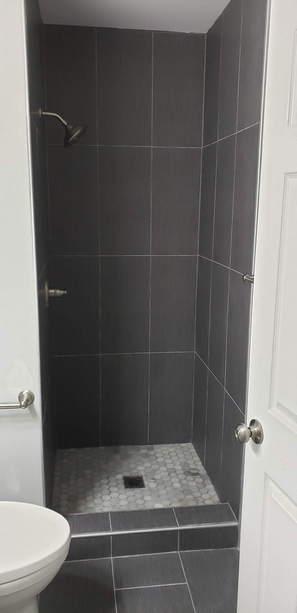 Remodelled shower finished in dark gray tile with a glass panel enclosure