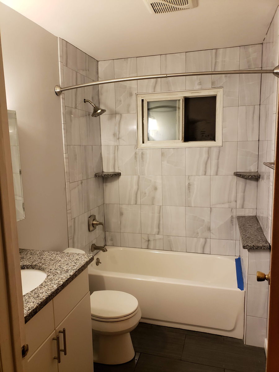 Marble-look tile tub surround with granite corner ledges and a new white tub