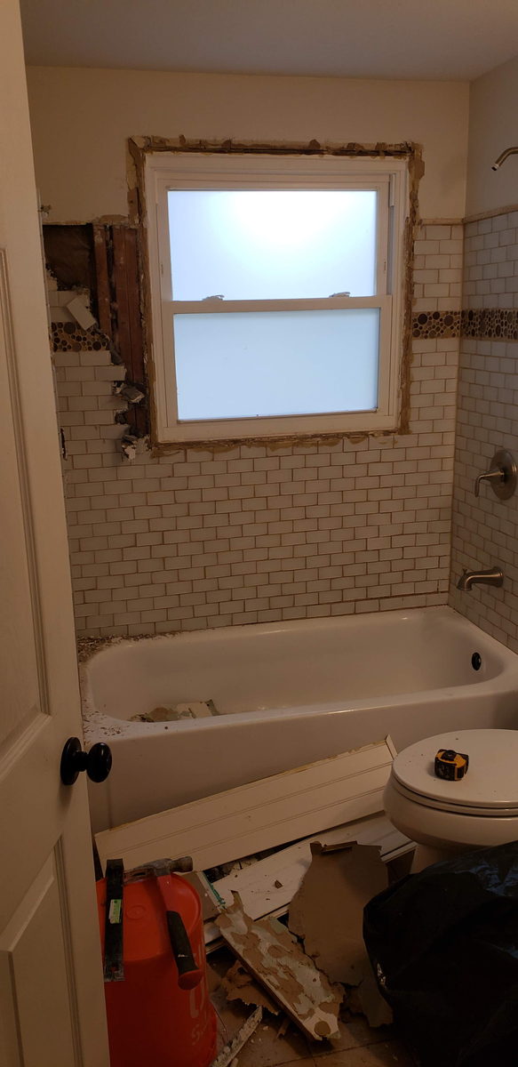 Bathroom mid-demolition with old wall tile stripped and debris on the floor