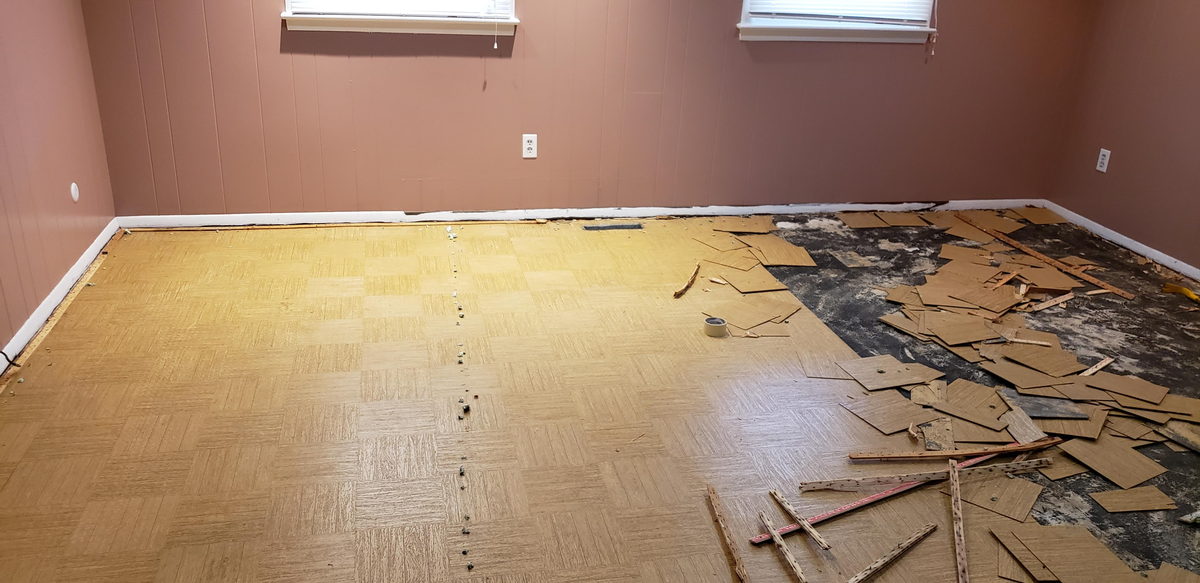 Old vinyl floor tile lifted and stacked mid-removal in an empty room