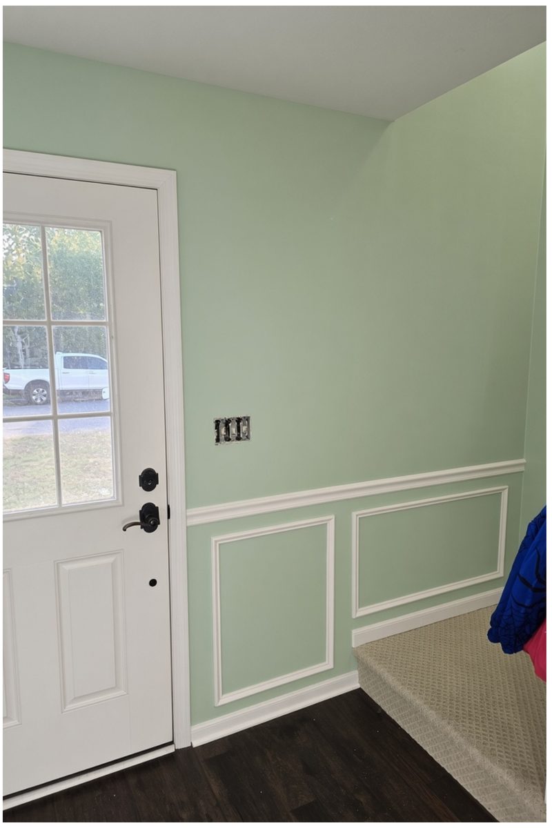 The same entry painted sage green with white picture-frame wainscot, chair rail, casing and door