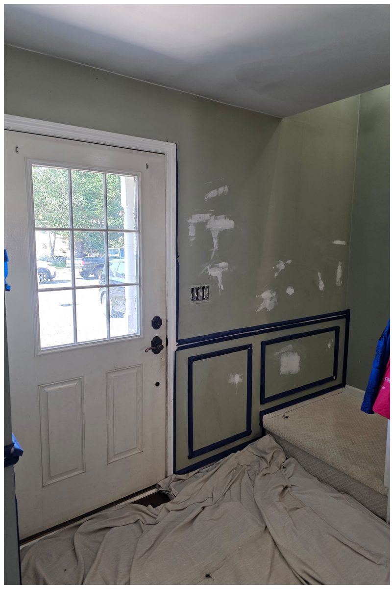 Entry with patched walls, picture-frame moulding laid out in tape, a drop cloth on the floor and a half-glass door