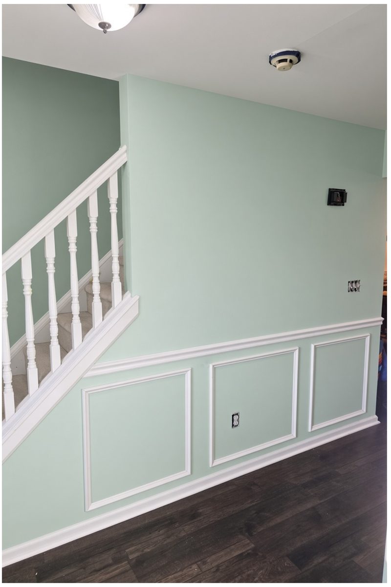 The same stair wall in sage green with white picture-frame wainscot, chair rail and balusters