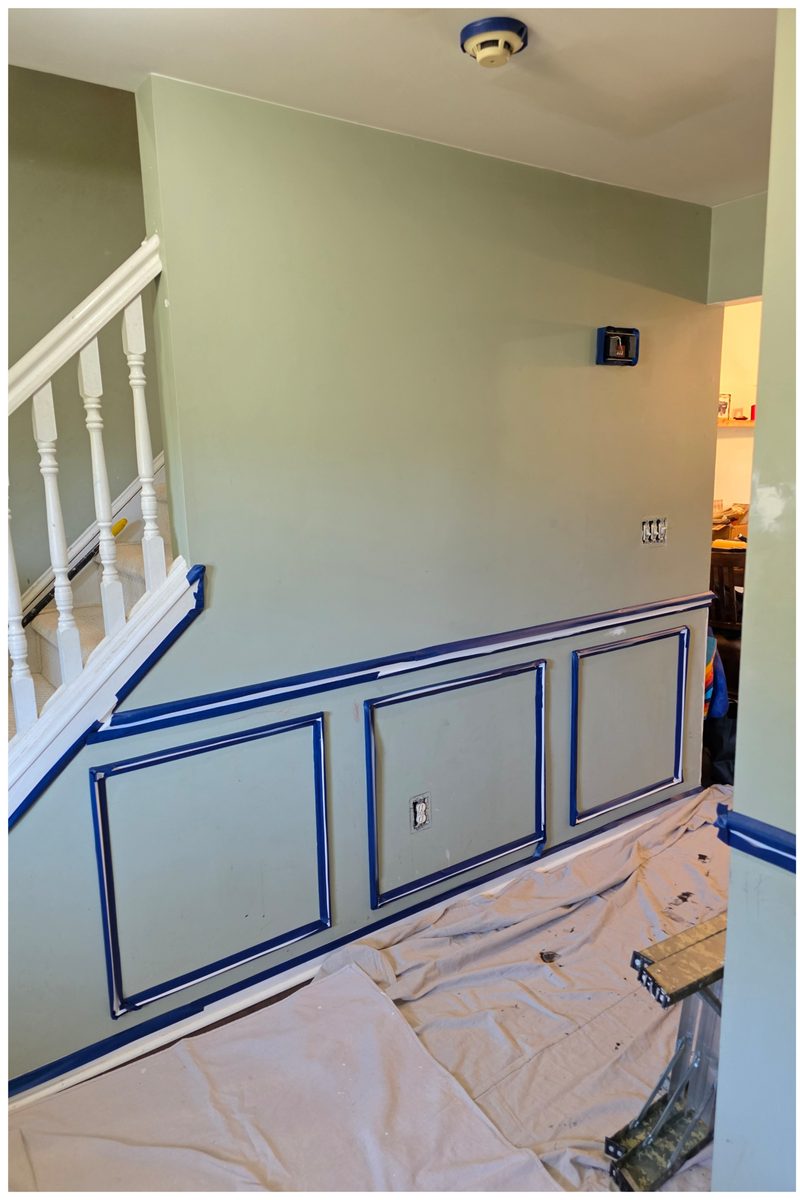 Foyer stair wall with picture-frame moulding laid out in tape and drop cloths on the floor