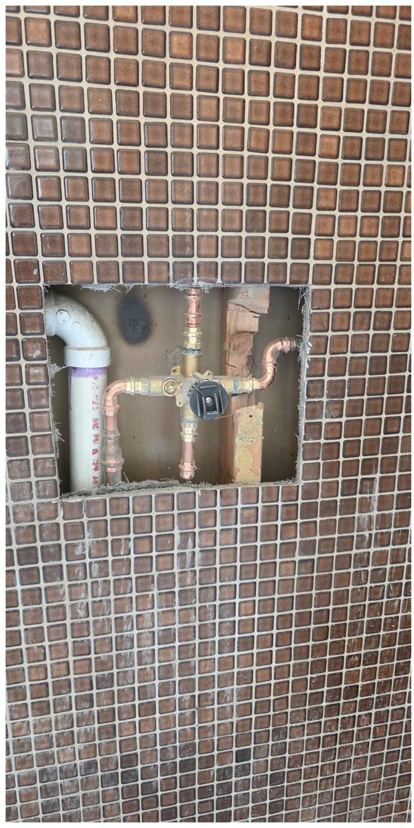 Shower wall with a section of brown mosaic tile removed and the new shower valve plumbed in