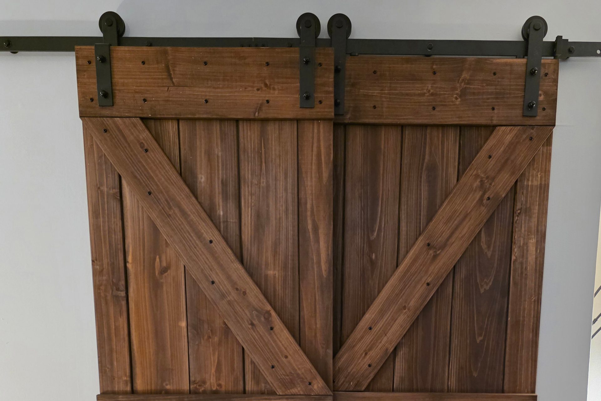 Pair of sliding barn doors with X bracing in a dark walnut stain, hung on a black top-mount track