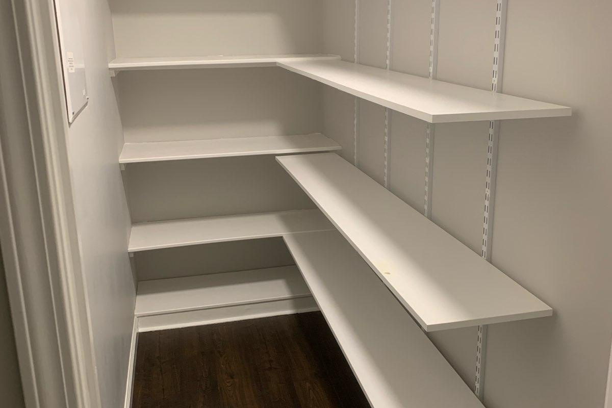 Custom white pantry shelving wrapping two walls with adjustable shelves