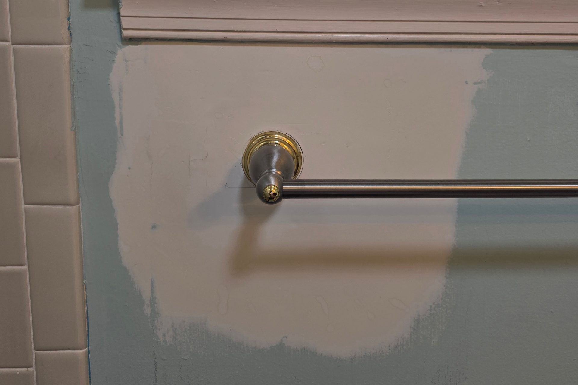 Drywall patch skim-coated and primed below a bathroom window, with the towel bar remounted