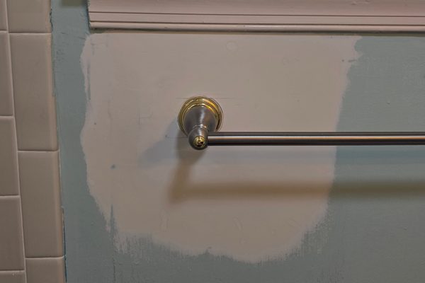 Drywall patch skim-coated and primed below a bathroom window, with the towel bar remounted