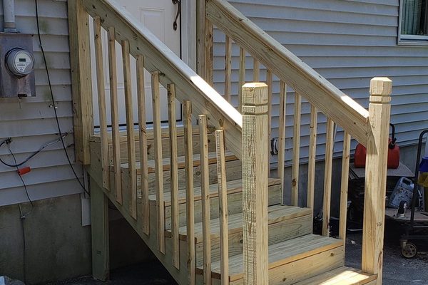 New pressure-treated entry stairs with turned balusters and a full handrail beside a side door