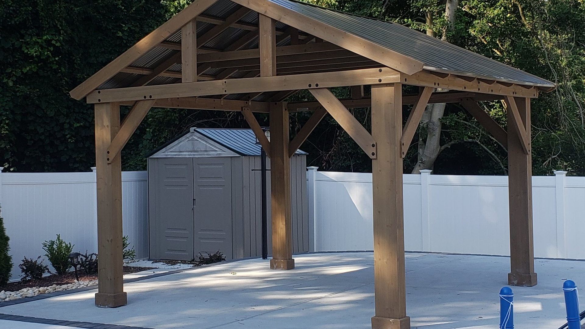 Finished timber-frame pavilion with a metal roof standing on a concrete pool patio