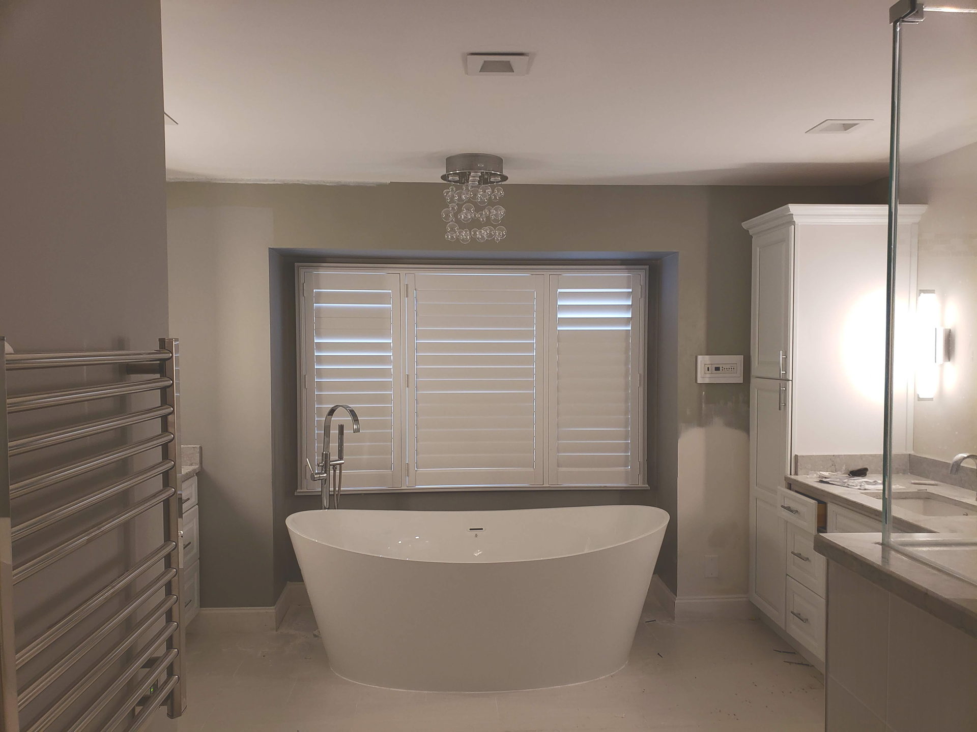 Master bathroom with a freestanding soaking tub set into a shuttered window recess and large-format floor tile