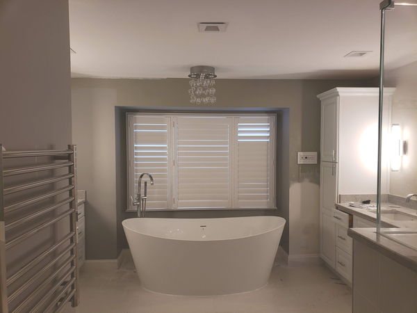 Master bathroom with a freestanding soaking tub set into a shuttered window recess and large-format floor tile