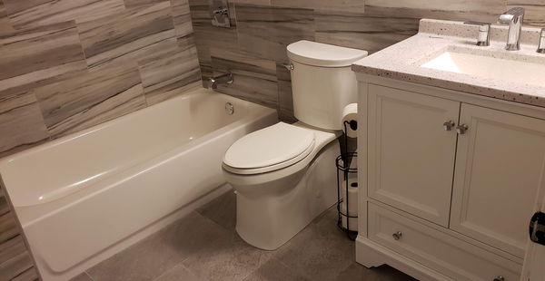 Wood-look tile tub surround beside a white vanity with a speckled quartz top