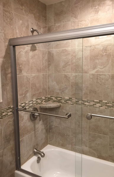 Travertine tile shower with a sliding glass door and a glass mosaic band