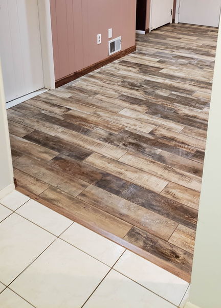 Wood-look plank tile floor meeting square white tile in a hallway