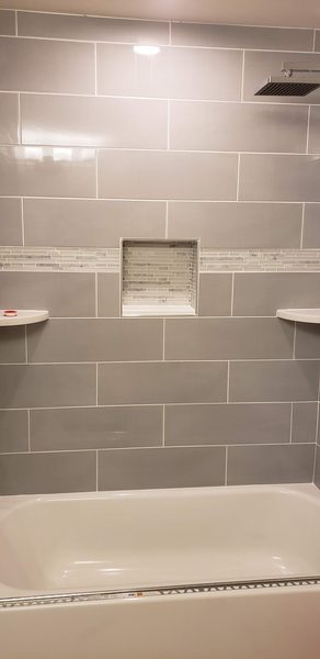 Tub and shower alcove in large gray subway tile with a marble mosaic accent band and a matching recessed niche