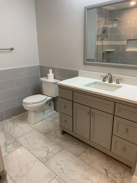 Remodelled bathroom with gray tile wainscot, marble-look floor and a gray vanity