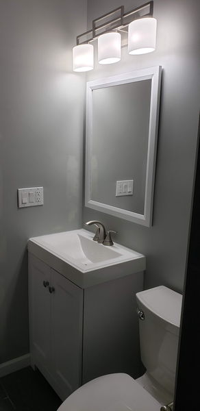 Gray vanity with a white top, framed mirror and a three-light fixture