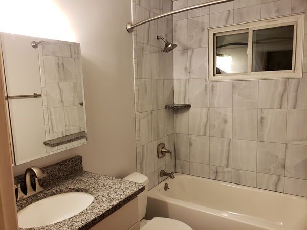 Marble-look tile shower wall beside a granite-topped vanity