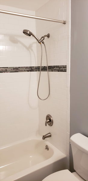 White subway tile tub surround with a dark glass mosaic accent band