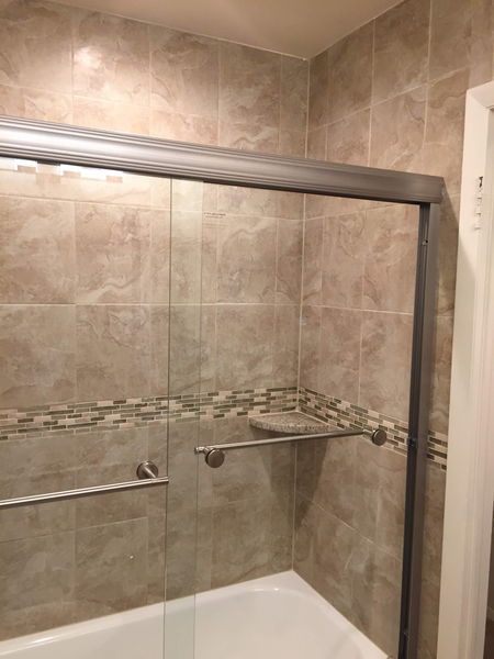 Travertine tile shower with sliding glass doors and a mosaic accent band