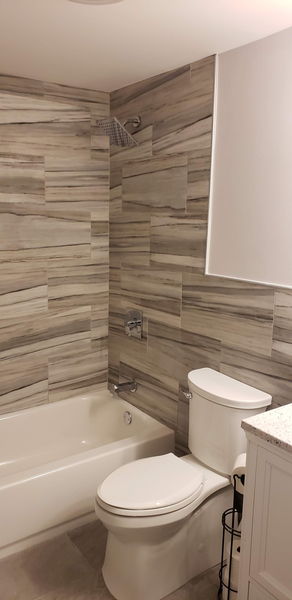 Large-format wood-look tile tub surround with chrome fixtures and a white tub