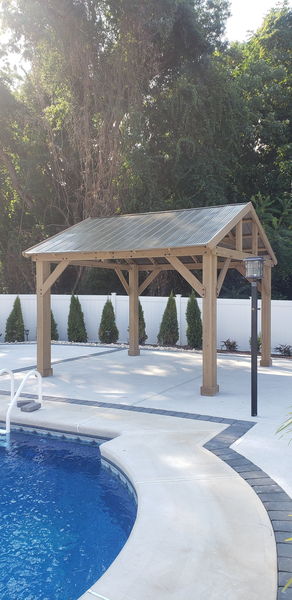 Cedar pavilion on a concrete pool patio with arborvitae along the fence