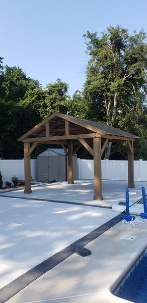 Timber-frame pavilion with a metal roof standing on a concrete patio