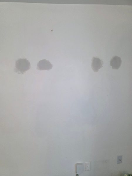 Four anchor holes patched and sanded flat on a white bedroom wall, ready for paint