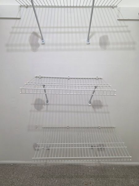 Closet wall with the old shelf-anchor holes patched flat and the white wire shelving re-hung