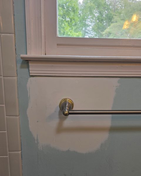 Drywall patch skim-coated and primed below a bathroom window, with the towel bar remounted
