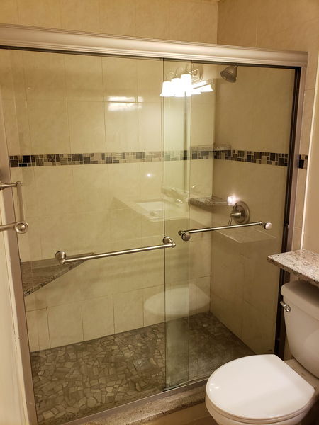Framed glass shower door installed against beige tile with a mosaic band
