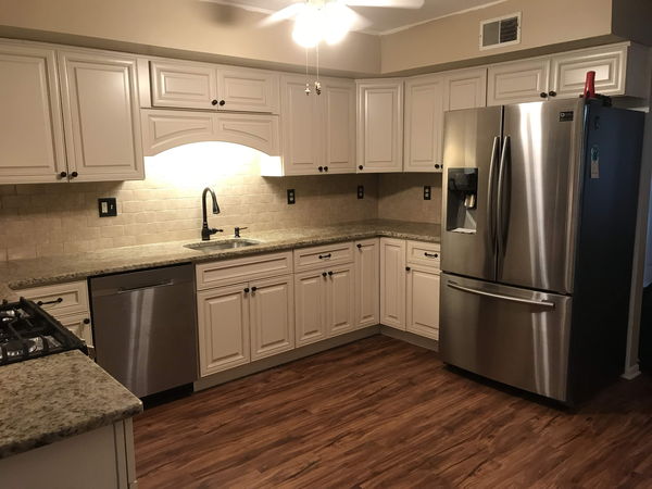 Granite counters and stone tile backsplash wrapping a cream cabinet run