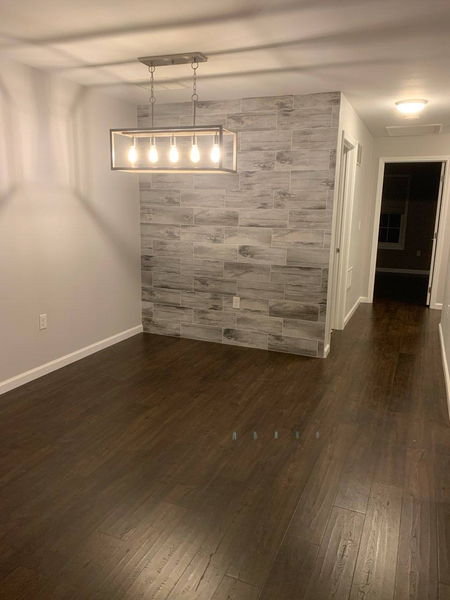 Wood-look tile accent wall above hardwood flooring with a linear pendant